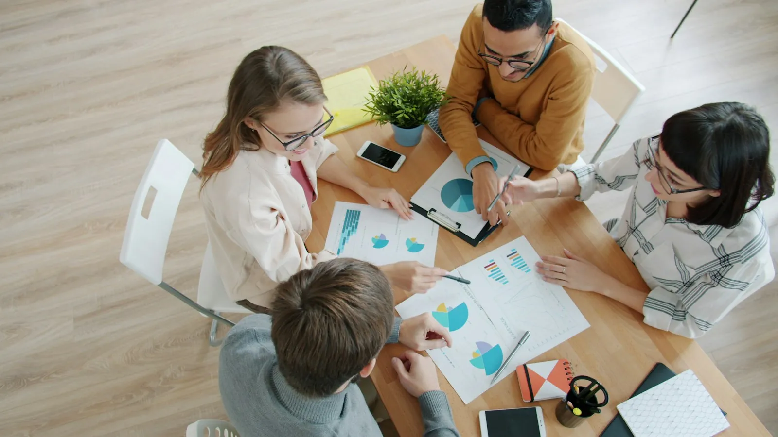 Four colleagues reviewing printed charts and graphs around a table